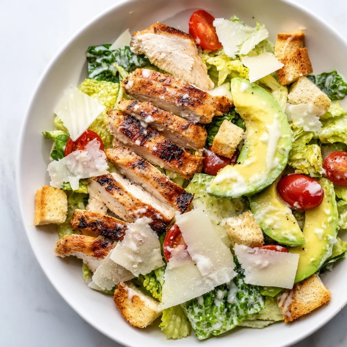 A close-up of a refreshing Chicken Caesar Salad with avocado, ready to be tossed with the zesty dressing.