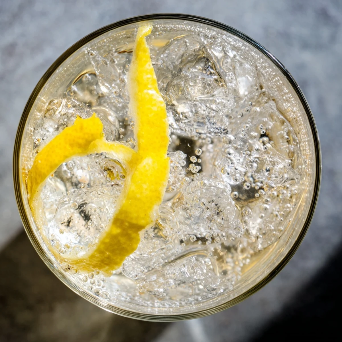 A vibrant Lemon Twist Cocktail garnished with a lemon peel twist sits over ice in a coupe glass, ready to sip.