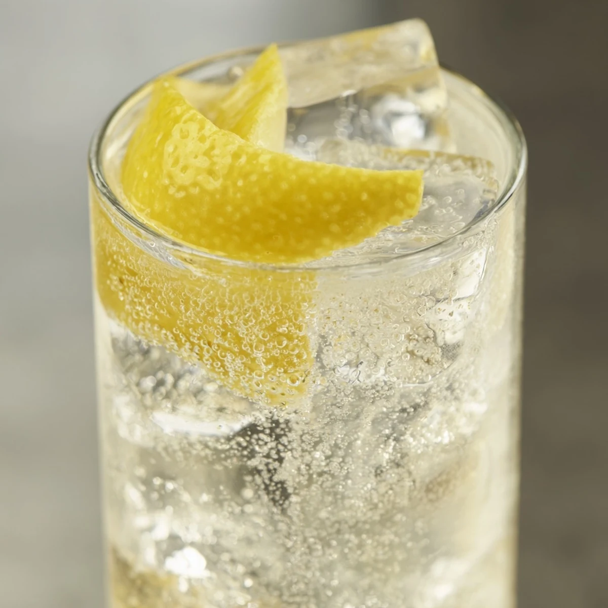The zesty Lemon Twist Cocktail is garnished with an aromatic lemon peel over ice in a coupe, a refreshing vegan drink.