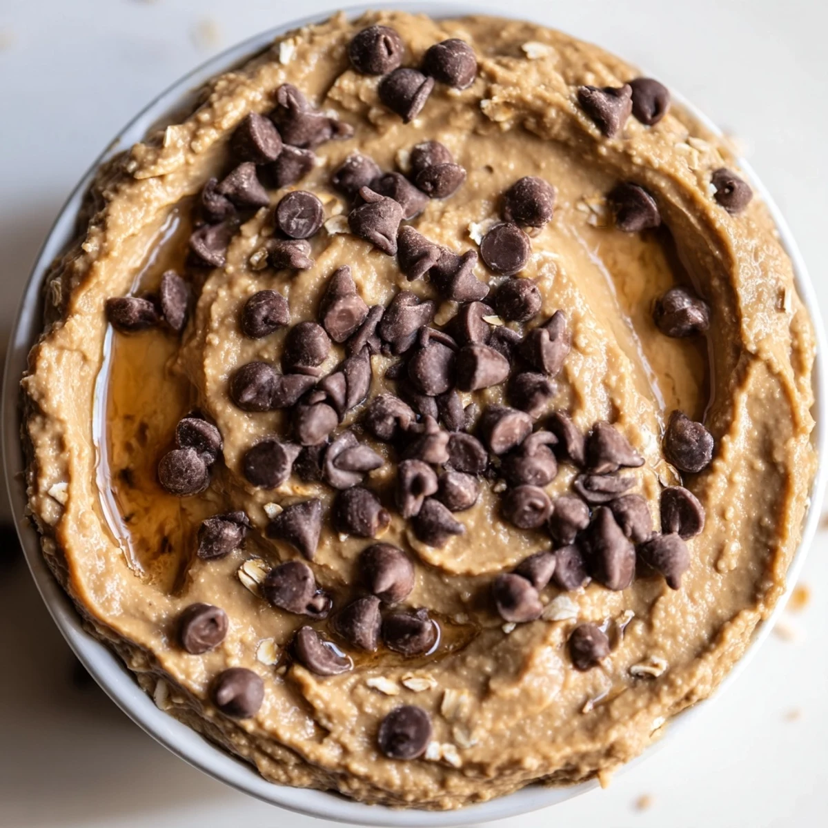 A bowl of Chocolate Chip Cookie Dough Hummus topped with chocolate chips, served with apple slices for dipping.