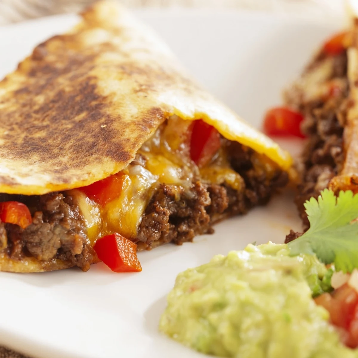 Golden-brown Beef Quesadillas with Salsa and Guacamole are cut into wedges on a rustic wooden board.