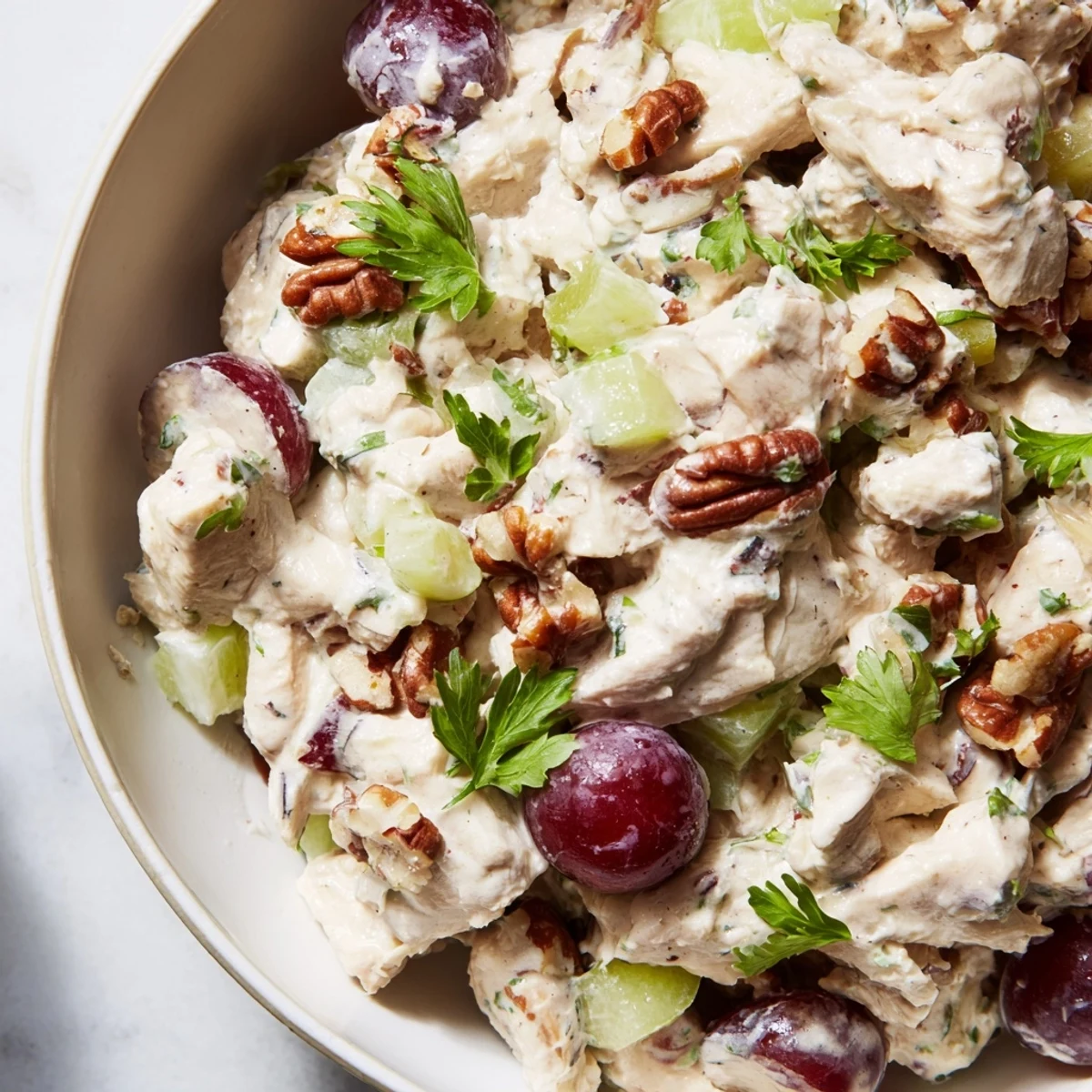 A close-up of creamy Chicken Salad with Pecans, featuring tender diced chicken, crunchy chopped pecans, crisp celery slices, and halved red grapes in a bowl.  