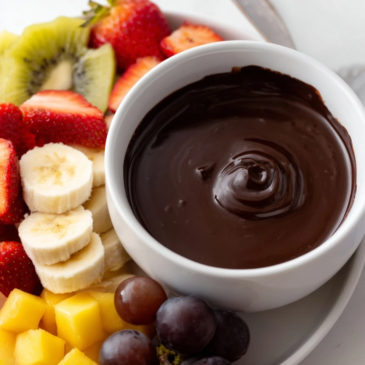 Glossy dark chocolate fondue streams over a vibrant platter of grapes, kiwi, and crisp apple slices.