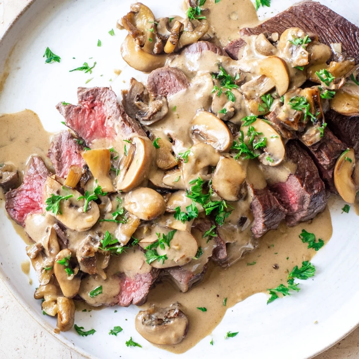 Sizzling steak slices in brandy-infused mushroom cream sauce with fresh parsley garnish on a skillet.