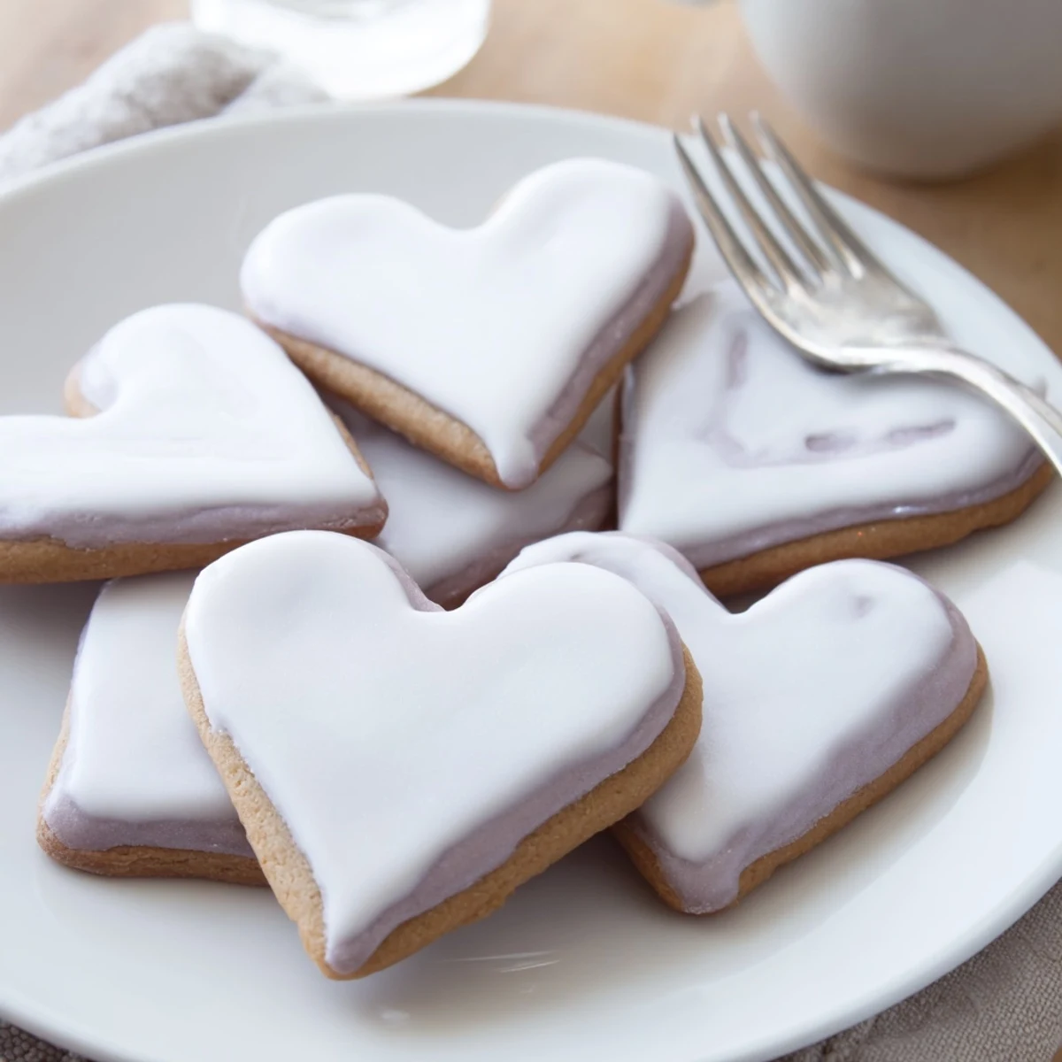 Freshly baked Heart Shaped Sugar Cookies with Royal Icing are arranged on a cooling rack, their glossy white icing gleaming under soft kitchen light.