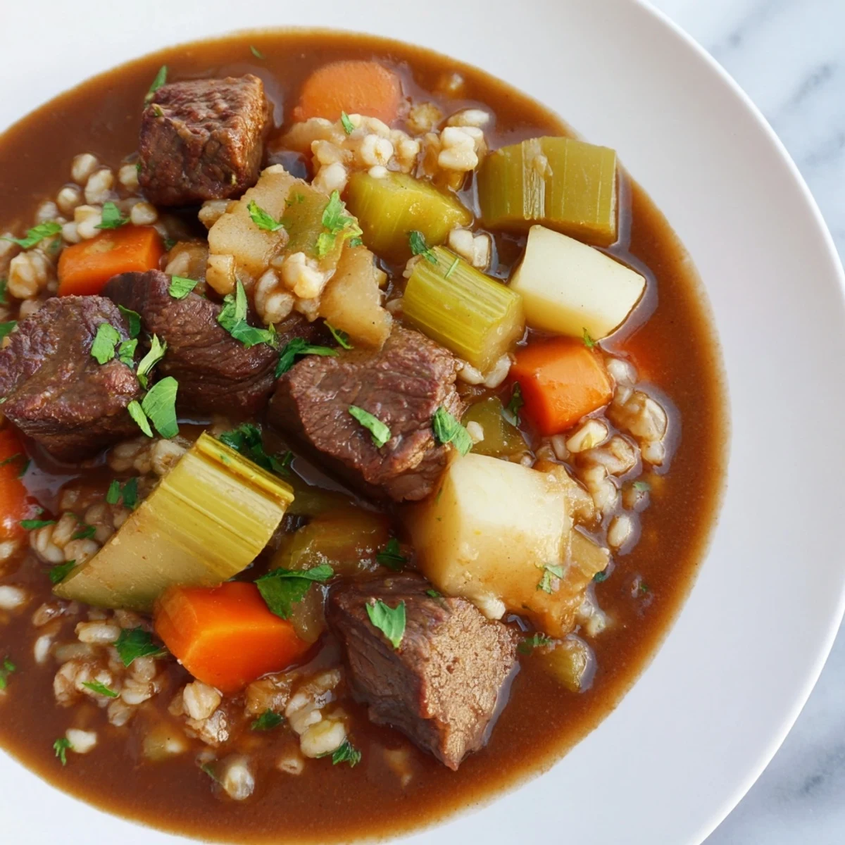 Close-up view of Irish Beef and Vegetable Stew with Barley in a rustic ceramic bowl, garnished with fresh parsley.