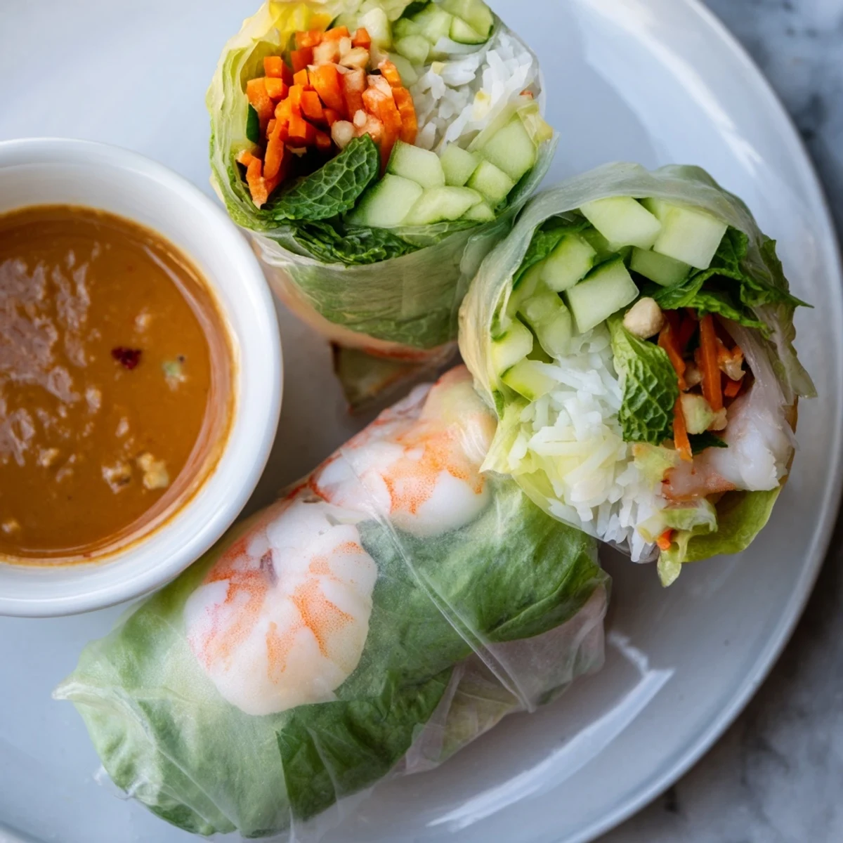 A close-up of Vietnamese Spring Rolls on a white plate, showcasing tender shrimp and vibrant mint leaves inside.