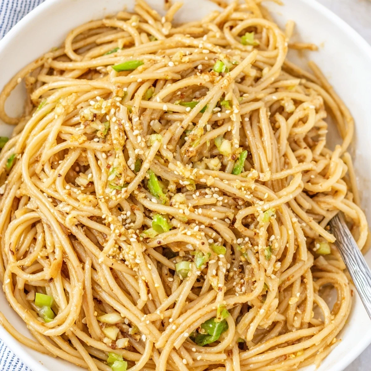 Steaming Garlic Noodles in a skillet, glistening with buttery sauce and topped with fresh scallions.