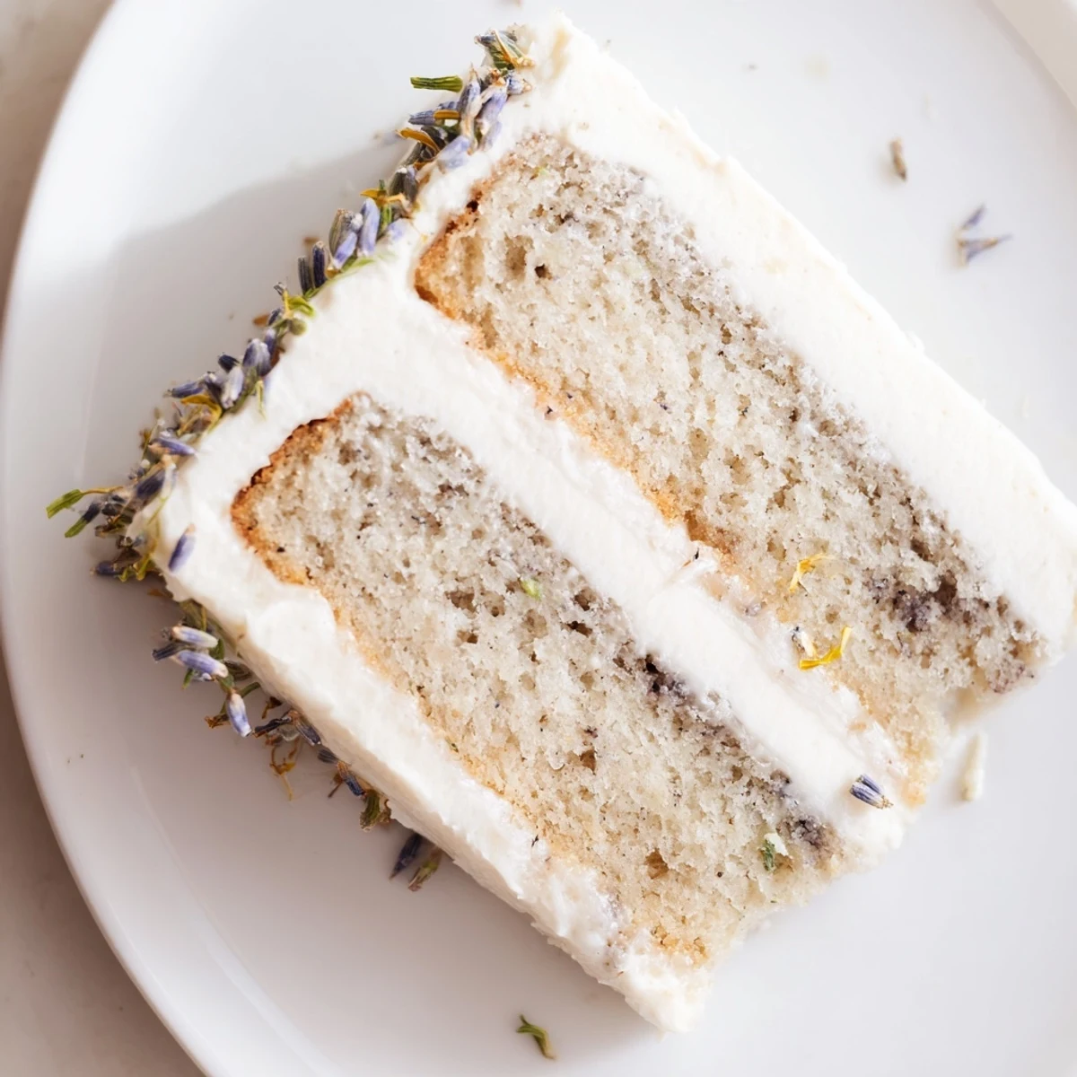 A slice of London Fog Cake with Earl Grey & Lavender reveals moist crumb and creamy vanilla bean frosting on a plate. 