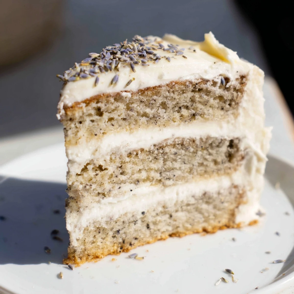 Close-up of London Fog Cake with Earl Grey & Lavender shows lavender garnish and drizzled frosting on a marble surface.