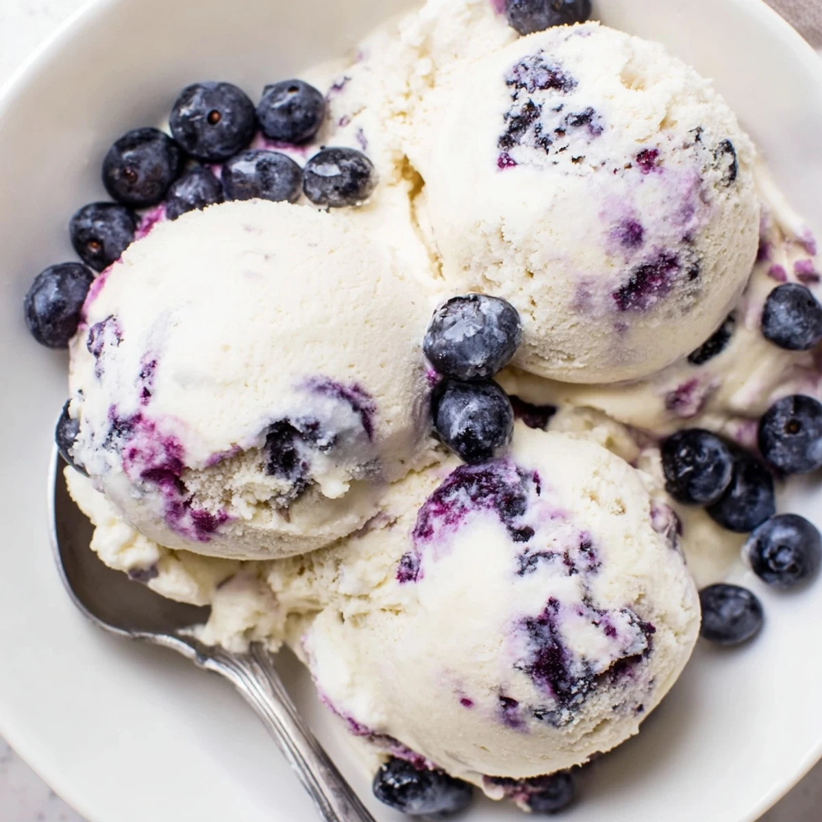 A scoop of Blueberry Cottage Cheese Ice Cream in a bowl, with fresh blueberries and a drizzle of honey on top.