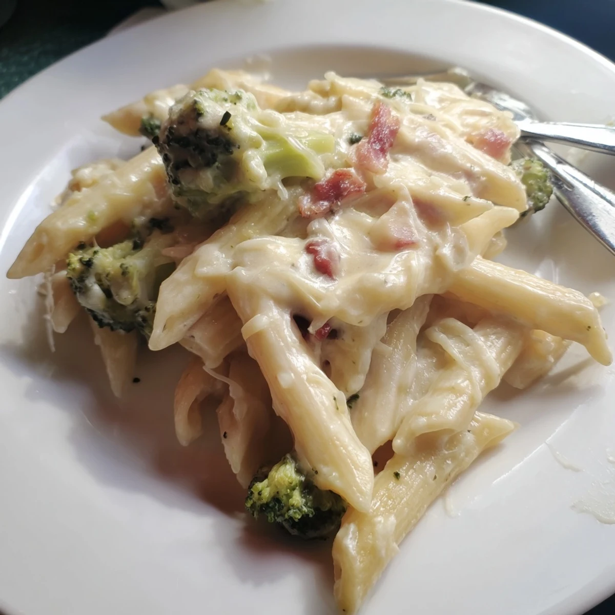 Creamy Bacon Broccoli and Parmesan Pasta served warm with golden, crispy bacon pieces and tender green broccoli florets on a fork.