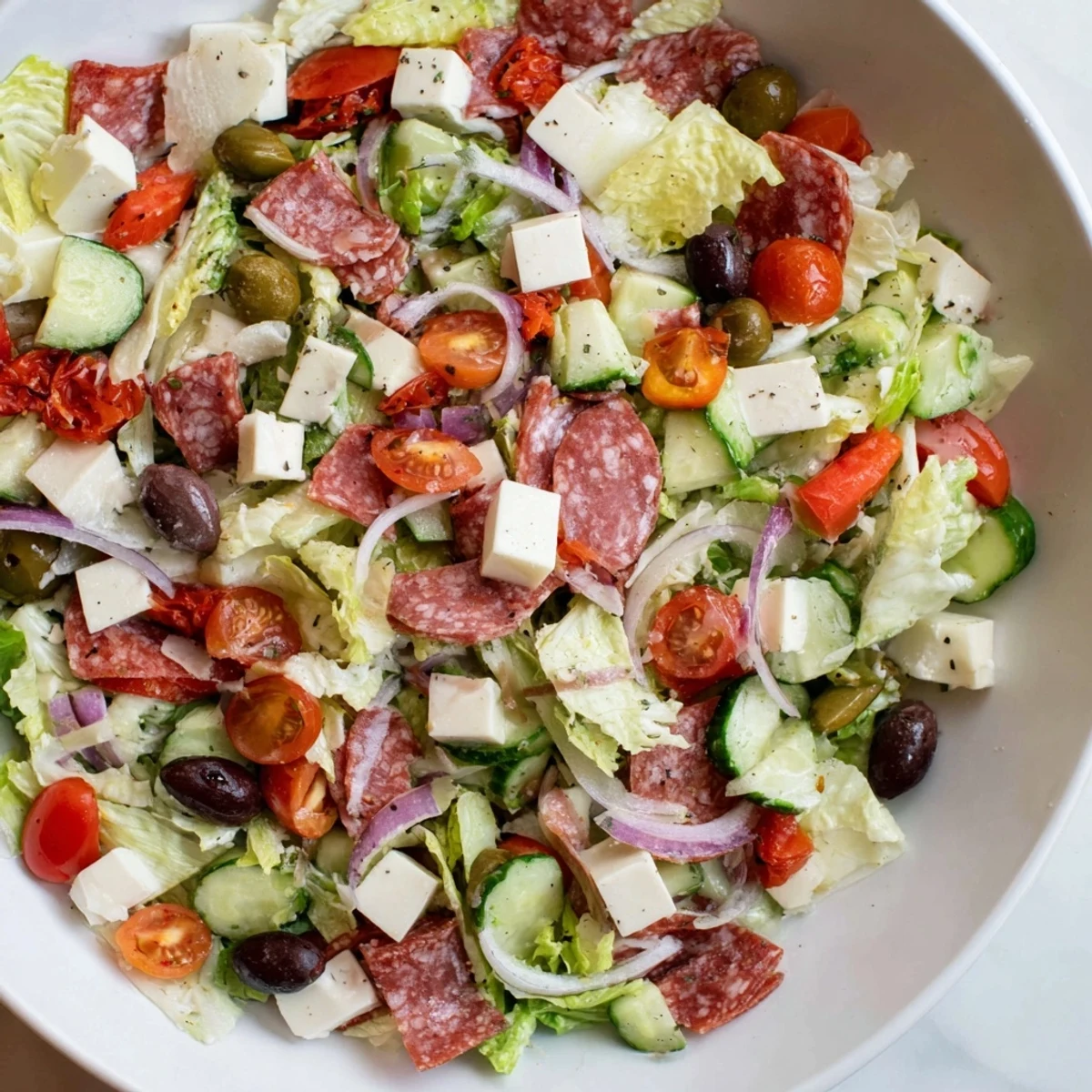 Colorful Italian chopped salad bowl with crisp romaine, salami, mozzarella, and olives drizzled with zesty homemade dressing.