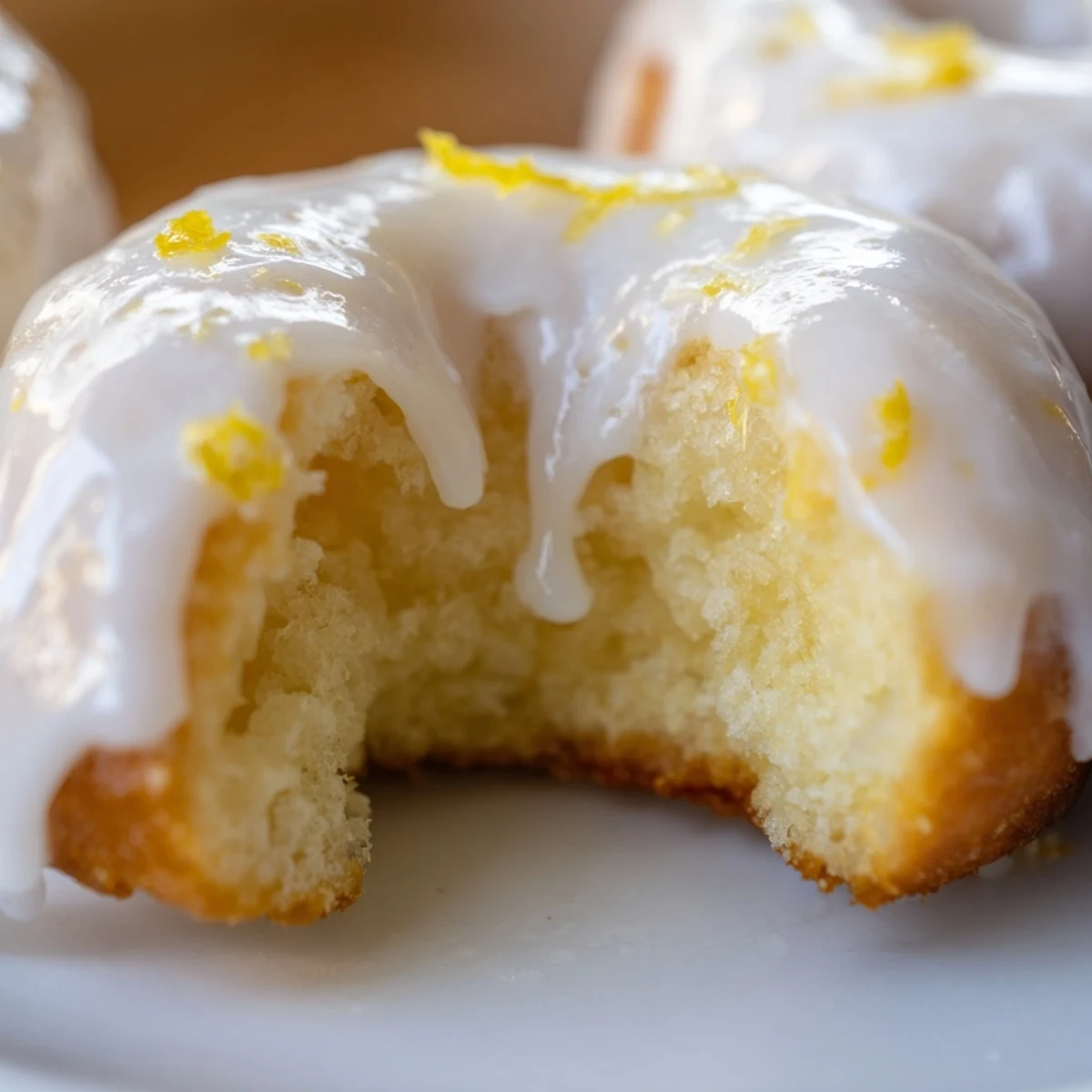 Golden glazed lemon mochi donuts with a crackly white icing top on a white plate