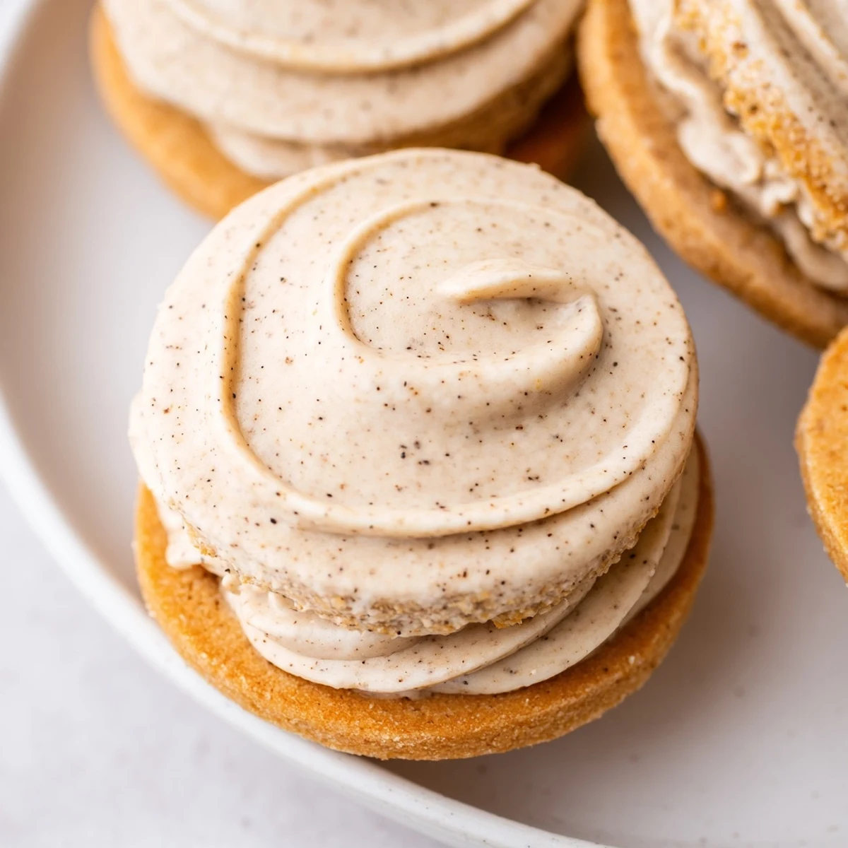 Homemade chai shortbread cookie sandwiches stacked on a plate with a warm cup of tea nearby