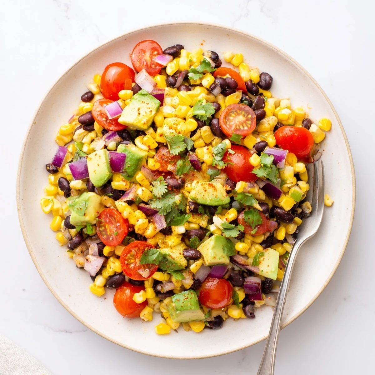 Colorful corn and black bean salad with fresh avocado in a white serving bowl