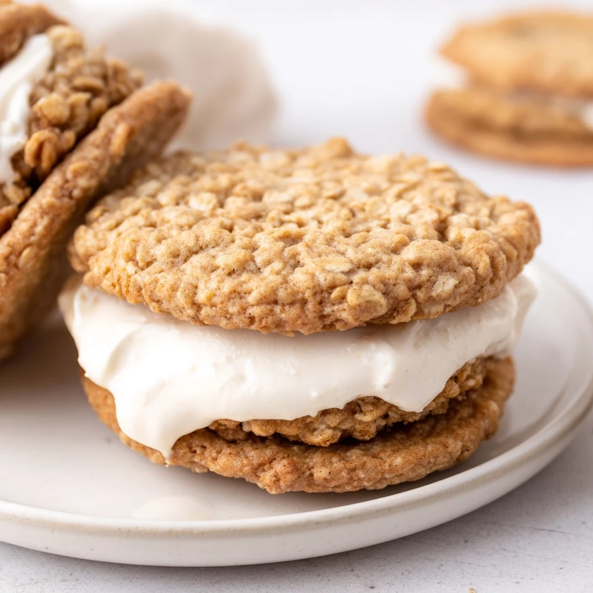 Two soft homemade oatmeal cream pies stacked on a white plate with generous vanilla frosting peeking between the chewy cookie layers