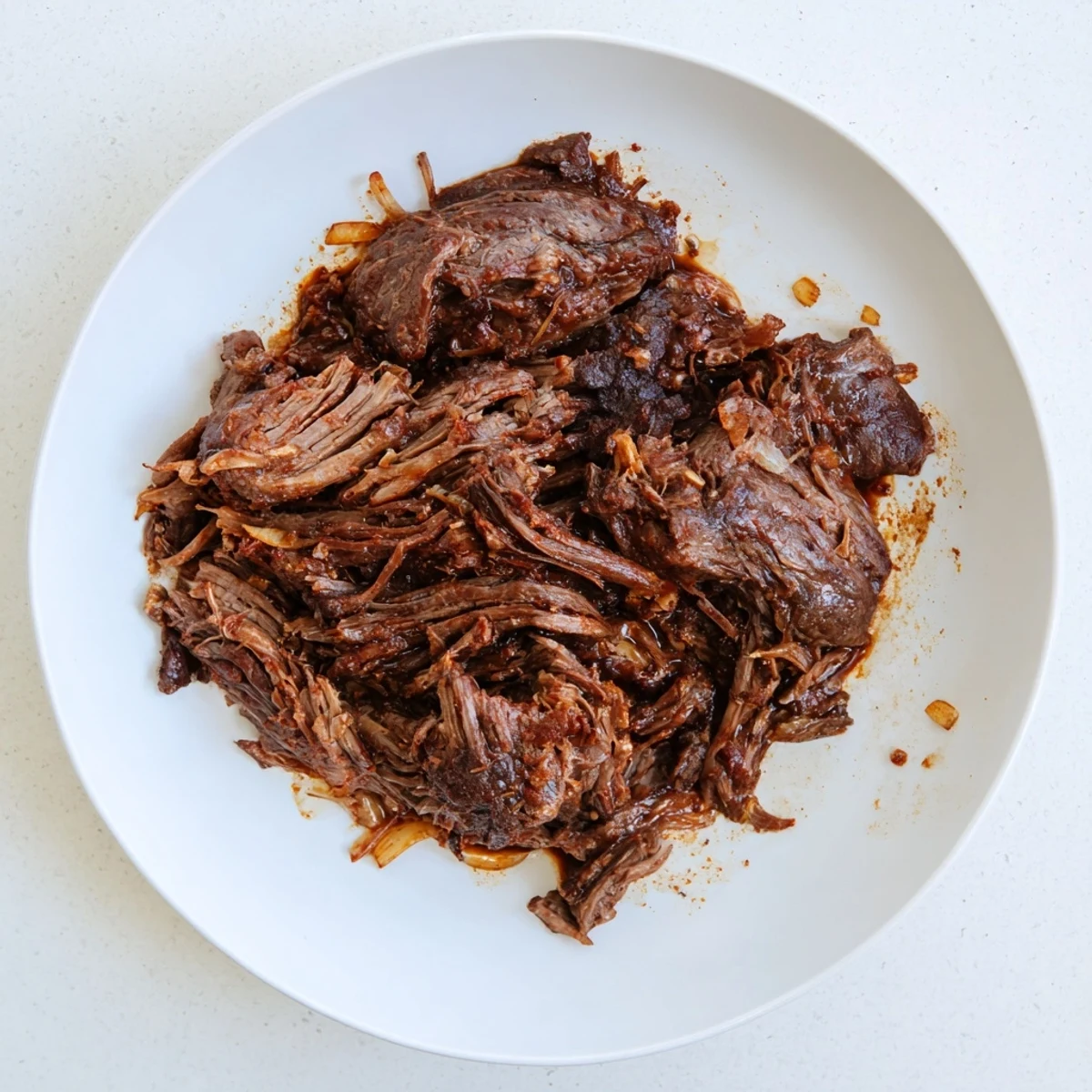 Tender Crock Pot shredded beef piled high on a plate with savory juices