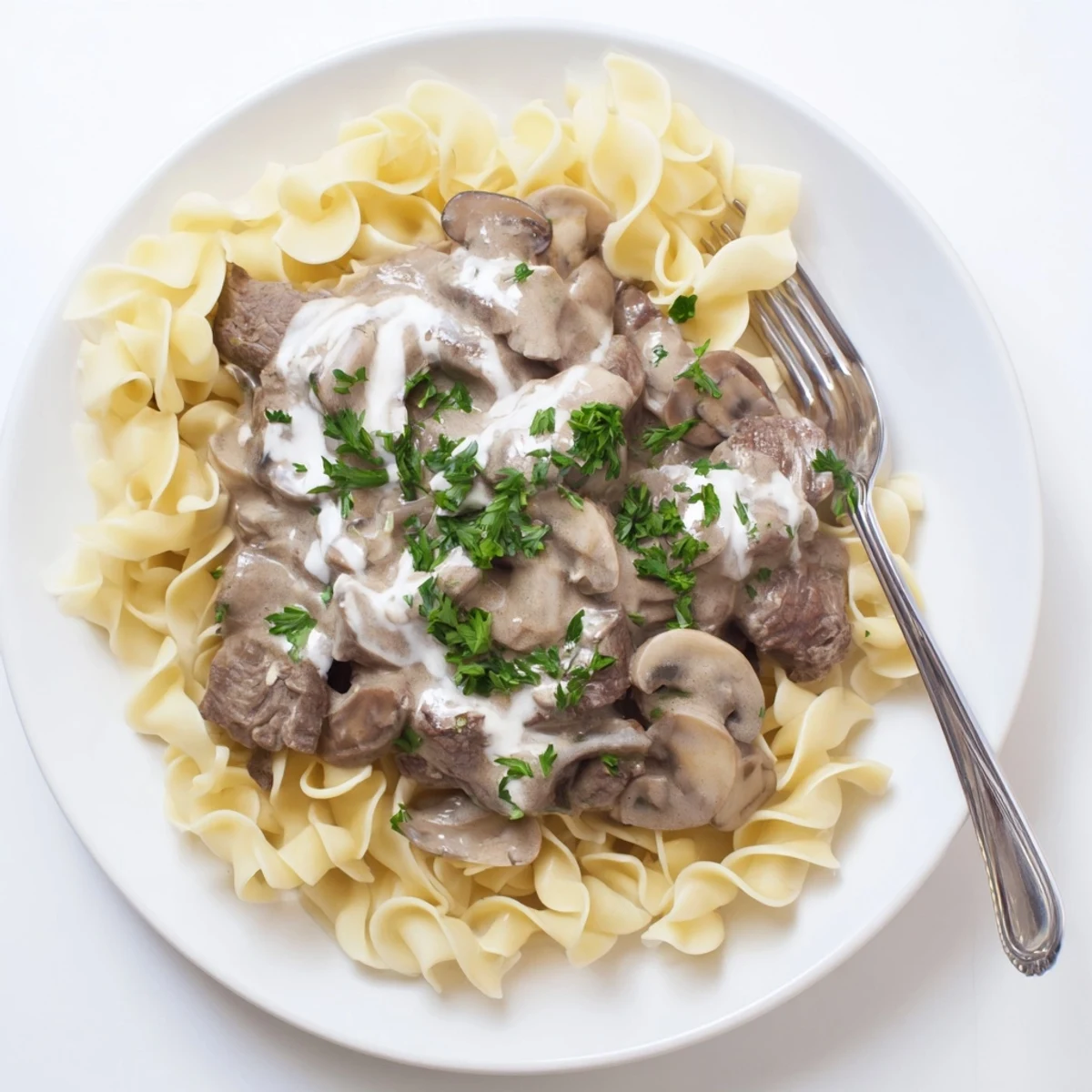 Creamy beef stroganoff with tender beef strips and mushrooms over egg noodles garnished with fresh parsley