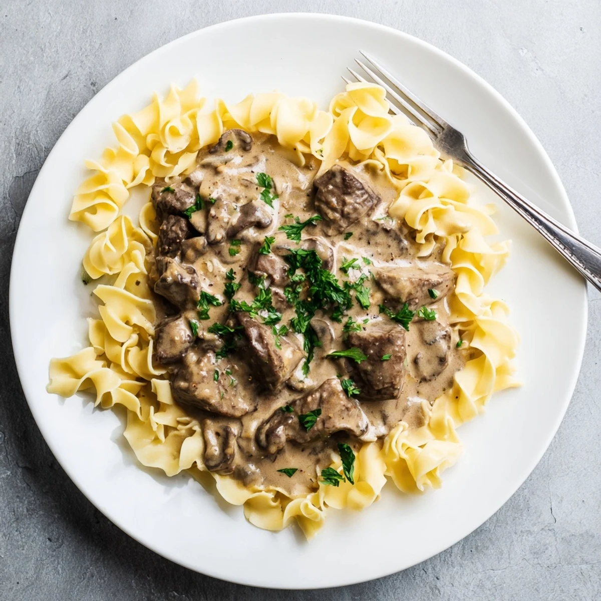 Classic beef stroganoff served on a white plate featuring rich sauce and parsley-topped egg noodles