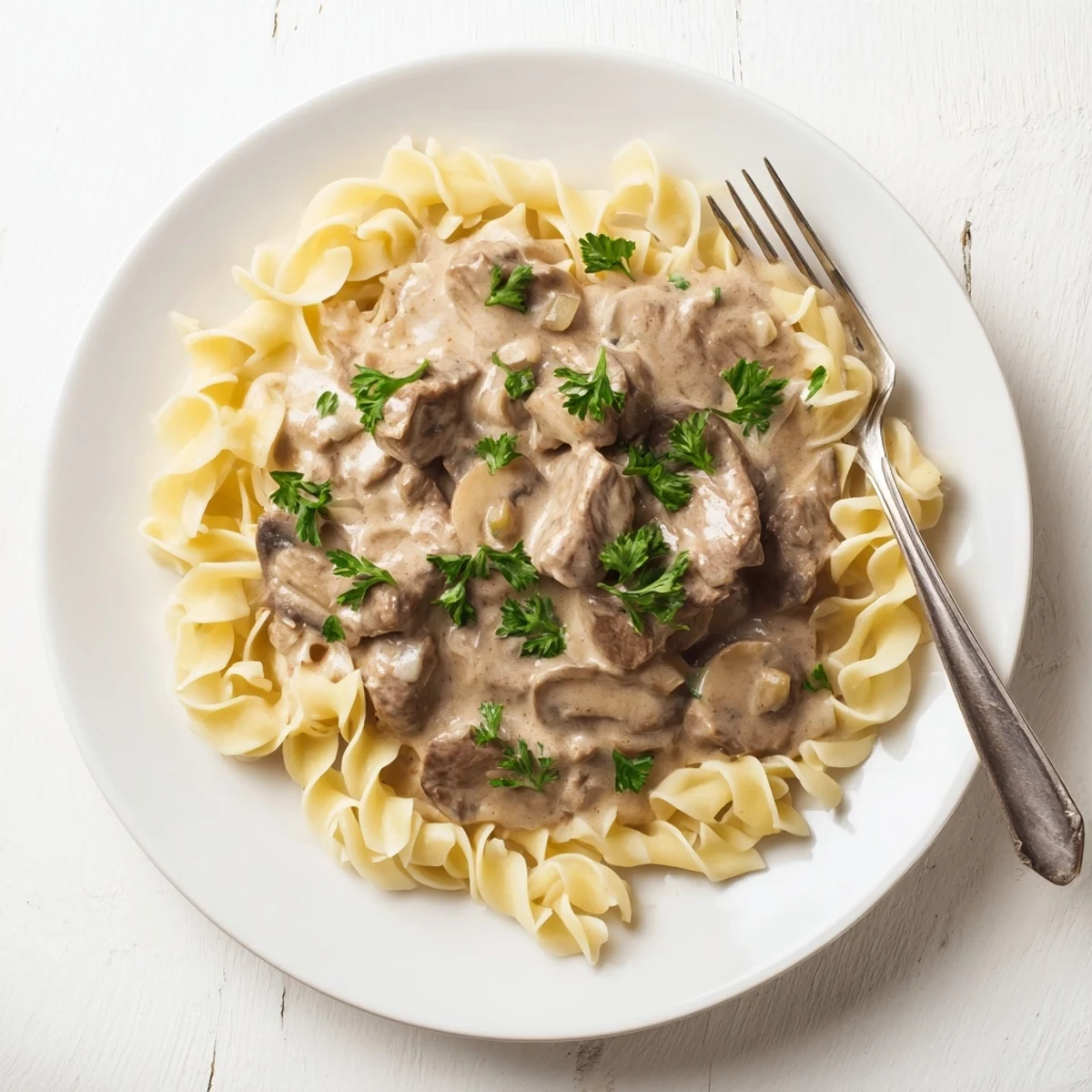 Homemade beef stroganoff showcasing golden mushroom sauce coating beef slices atop a bed of noodles