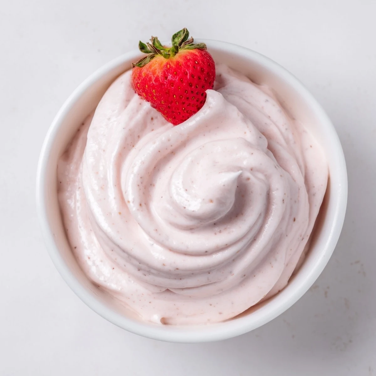 Creamy pink Frozen Strawberry Dole Whip Delight swirled into a glass bowl topped with fresh strawberry slices