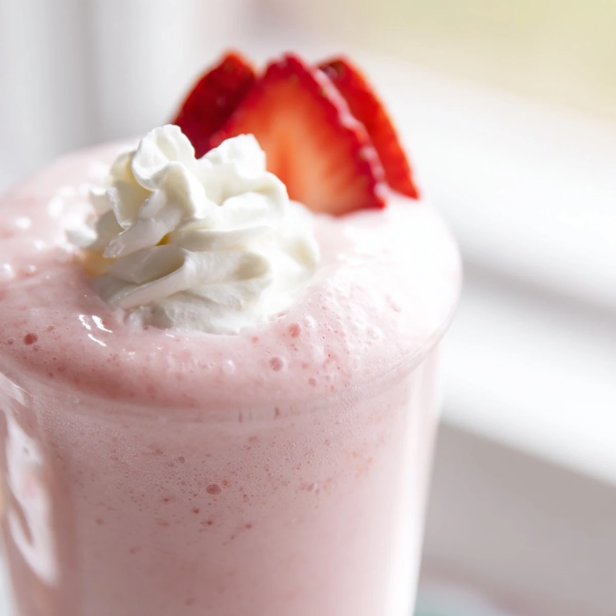Blended ice-cold strawberry cream Frappuccino displaying pink frothy texture with garnish on glass rim