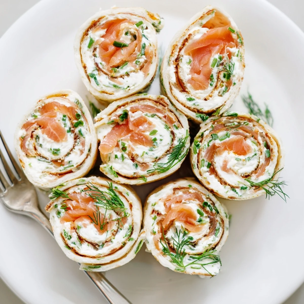 Close-up of bite-sized smoked salmon roll ups showing layers of tender fish, smooth cheese, and green chives