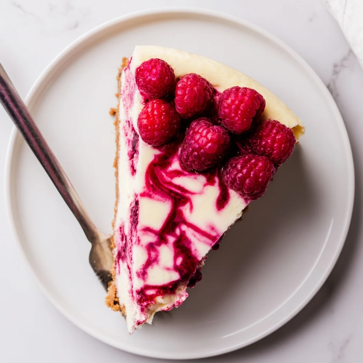 Creamy raspberry cheesecake slice with vibrant red swirls on a graham cracker crust