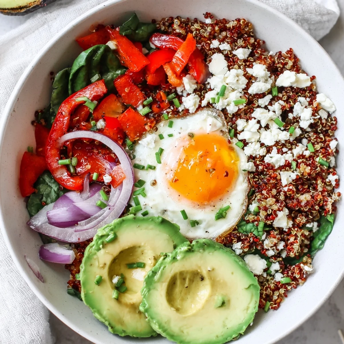 Golden fried egg resting atop fluffy savory quinoa breakfast bowl with colorful sautéed vegetables