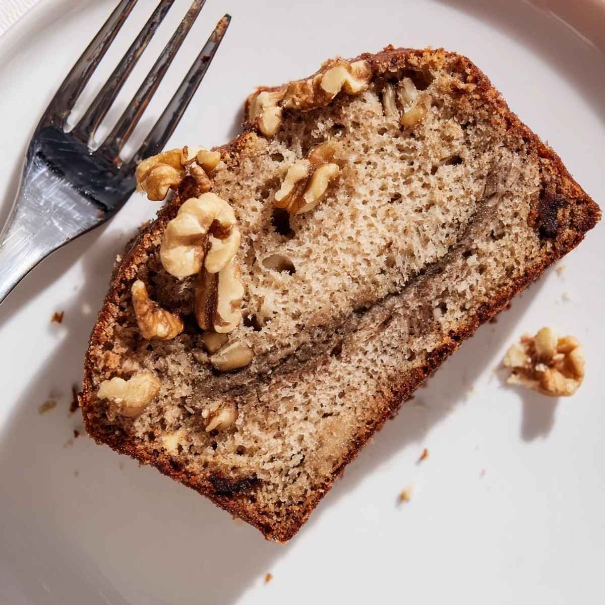 Thick slice of moist banana bread with chopped walnuts and ribbons of cinnamon on a white plate