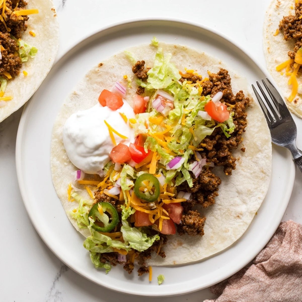Crispy beef Blackstone smash tacos topped with fresh lettuce, diced tomatoes, and creamy sour cream
