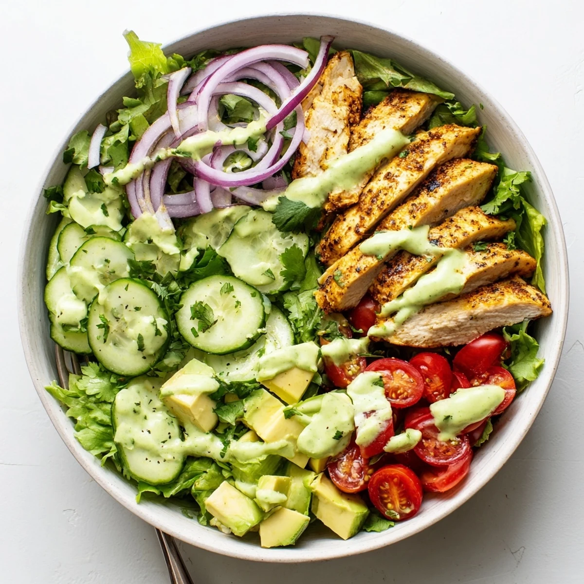 Fresh vegetable salad bowl topped with juicy seasoned grilled chicken and smooth homemade avocado dressing