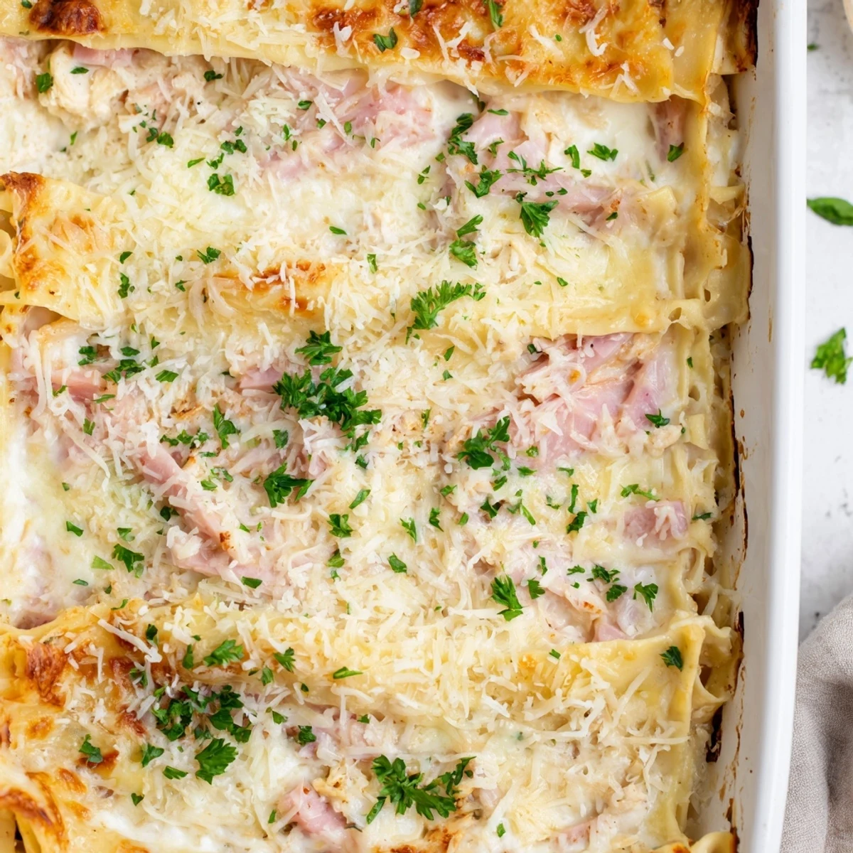 Sliced chicken cordon bleu lasagna topped with golden mozzarella and garnished with fresh parsley on a white serving plate