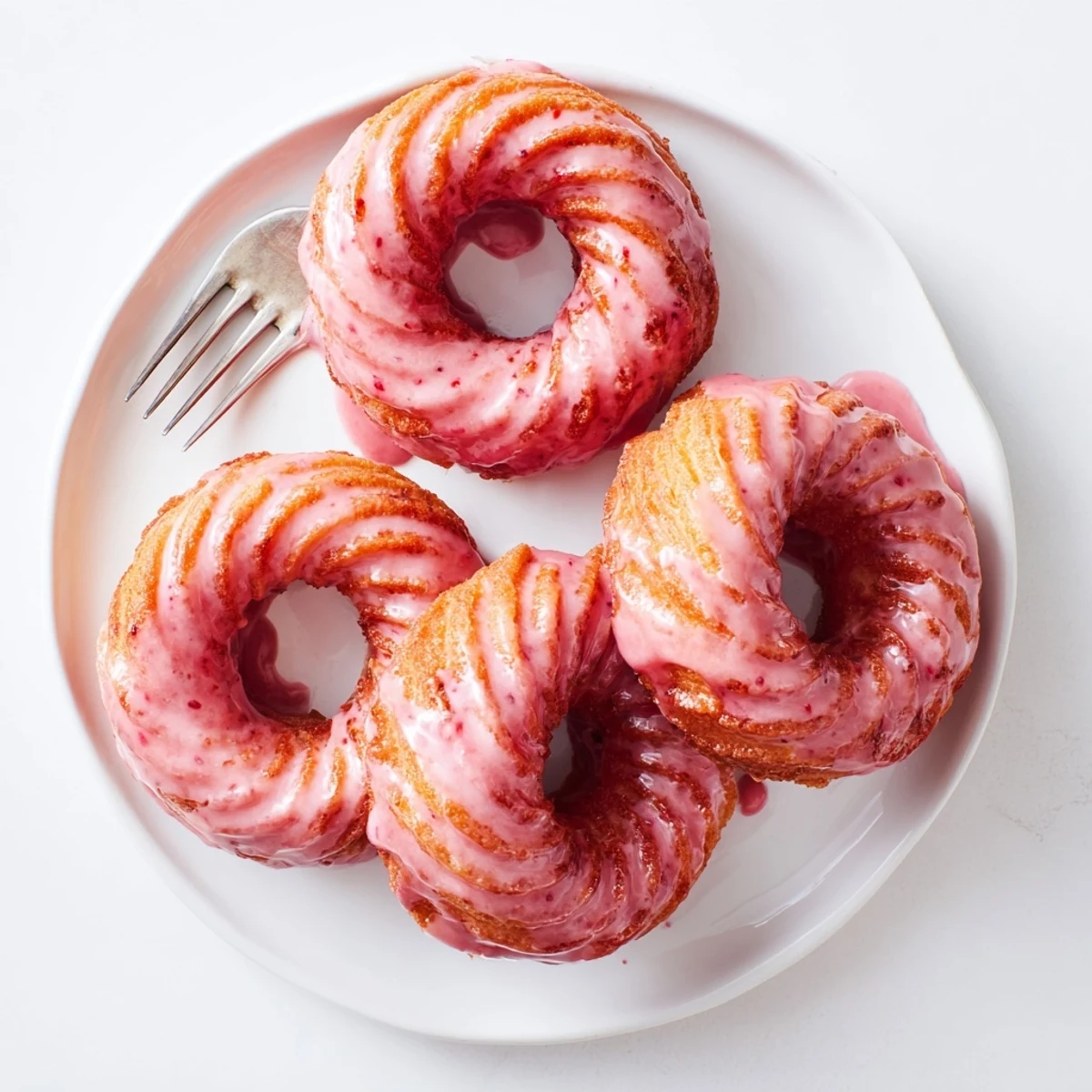 Golden strawberry glazed French crullers with glossy pink icing on a wire cooling rack.