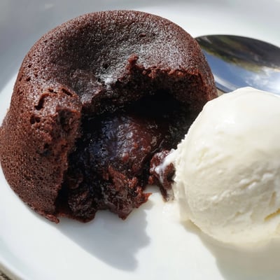 Chocolate Lava Cakes with Vanilla Bean Ice Cream are plated next to a fresh raspberry, highlighting the rich, gooey chocolate dessert for a sweet treat.