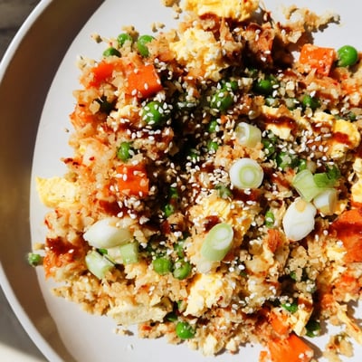 A close-up of Cauliflower Fried Rice with Kimchi and Eggs topped with sesame seeds and green onions on a white plate.