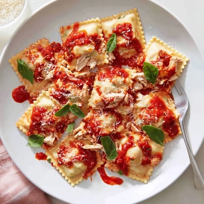 Freshly cooked Chicken and Mushroom Ravioli with Simple Tomato Sauce steaming beside a glass of red wine on a rustic wooden table.